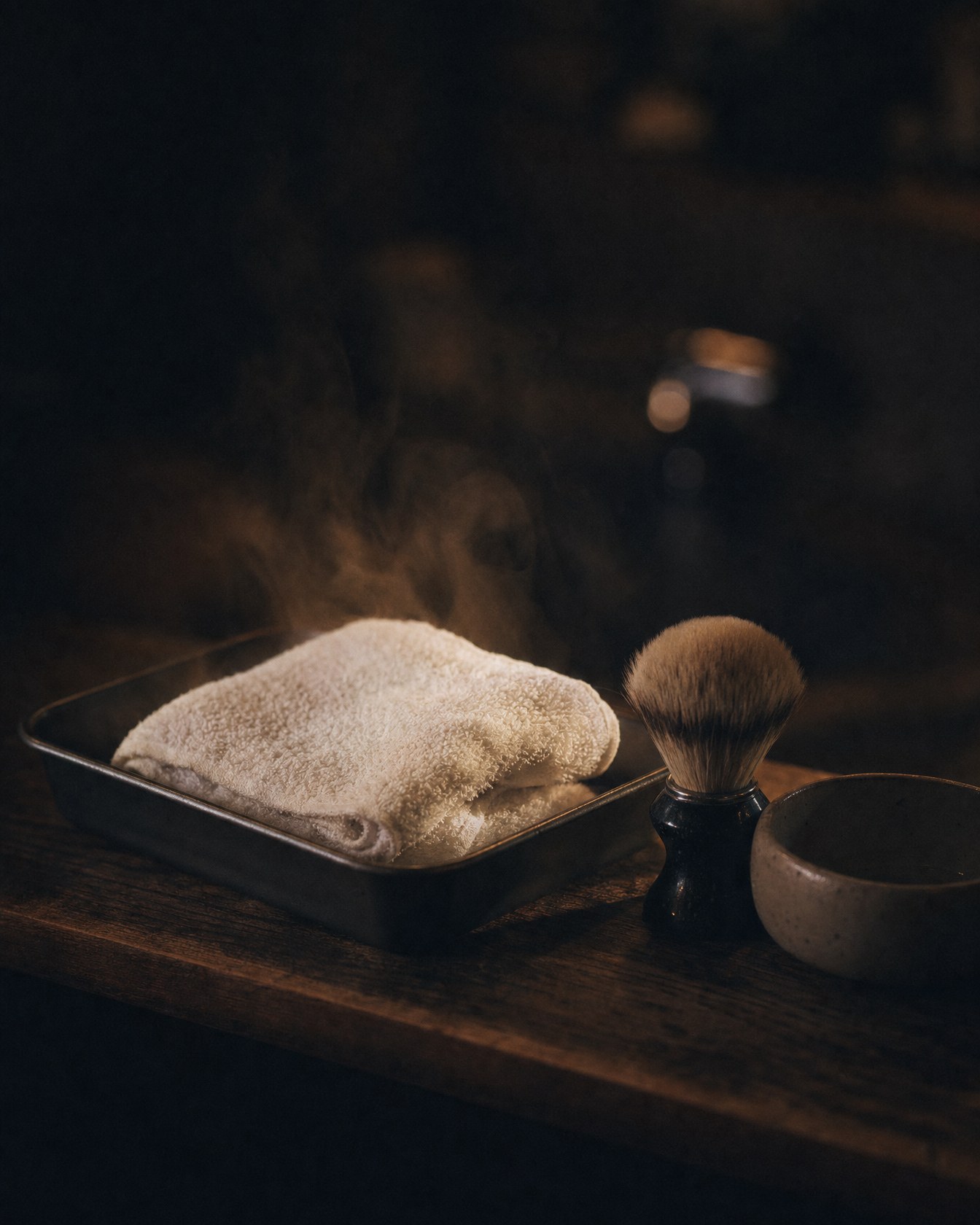 A hot towel steaming in a tray beside a shaving brush